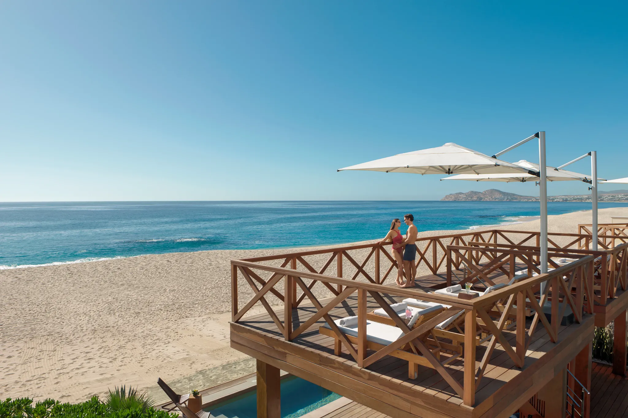 Couple standing on a luxury beach cabana deck overlooking the Sea of Cortez at Dreams Los Cabos Suites Golf Resort & Spa.