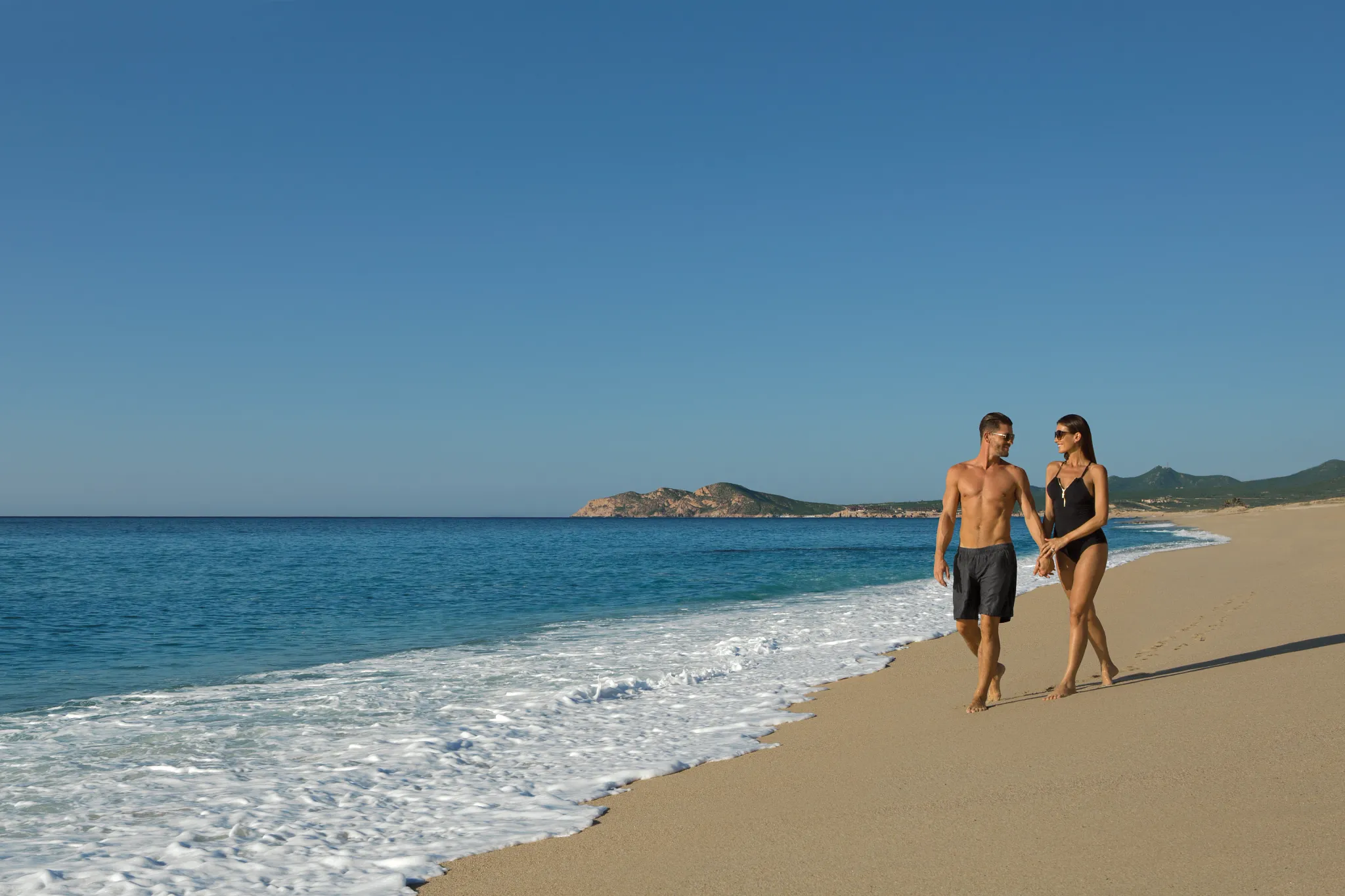 Couple walking hand in hand along the beach at Dreams Los Cabos Suites Golf Resort & Spa.