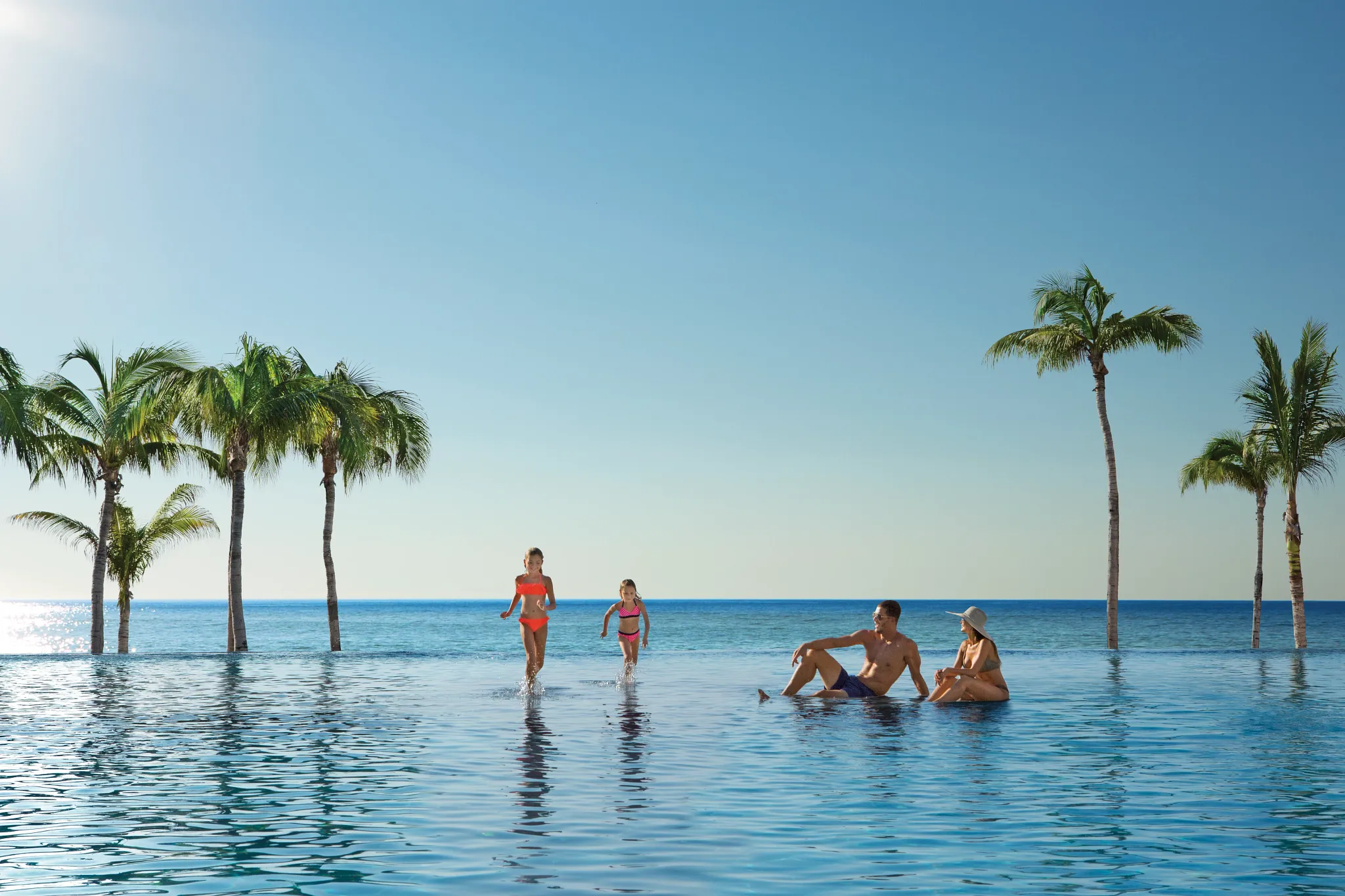 Family relaxing and playing in the oceanfront infinity pool at Dreams Los Cabos Suites Golf Resort & Spa.