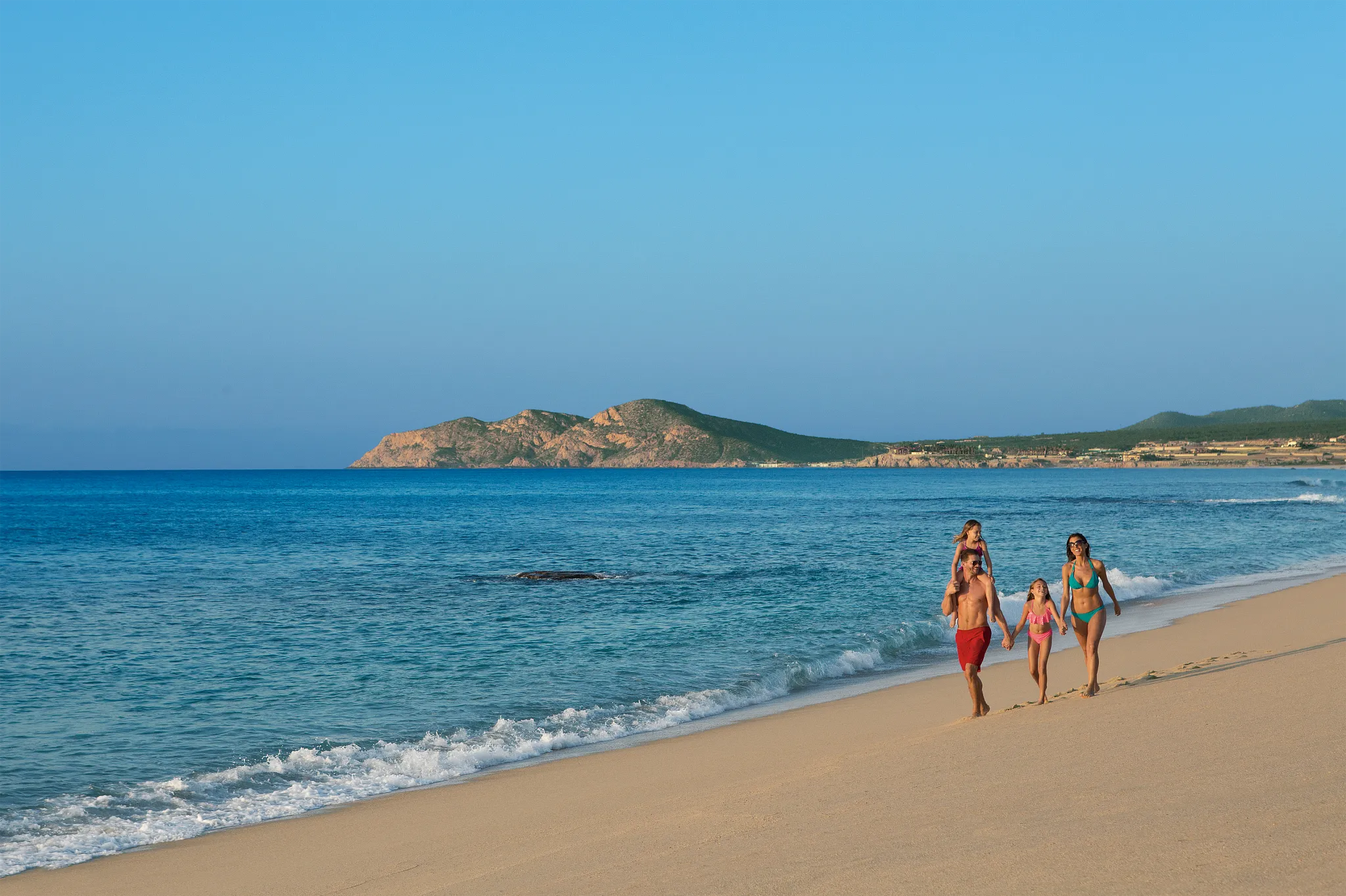 Family walking together along the sandy beach at Dreams Los Cabos Suites Golf Resort & Spa in Los Cabos.