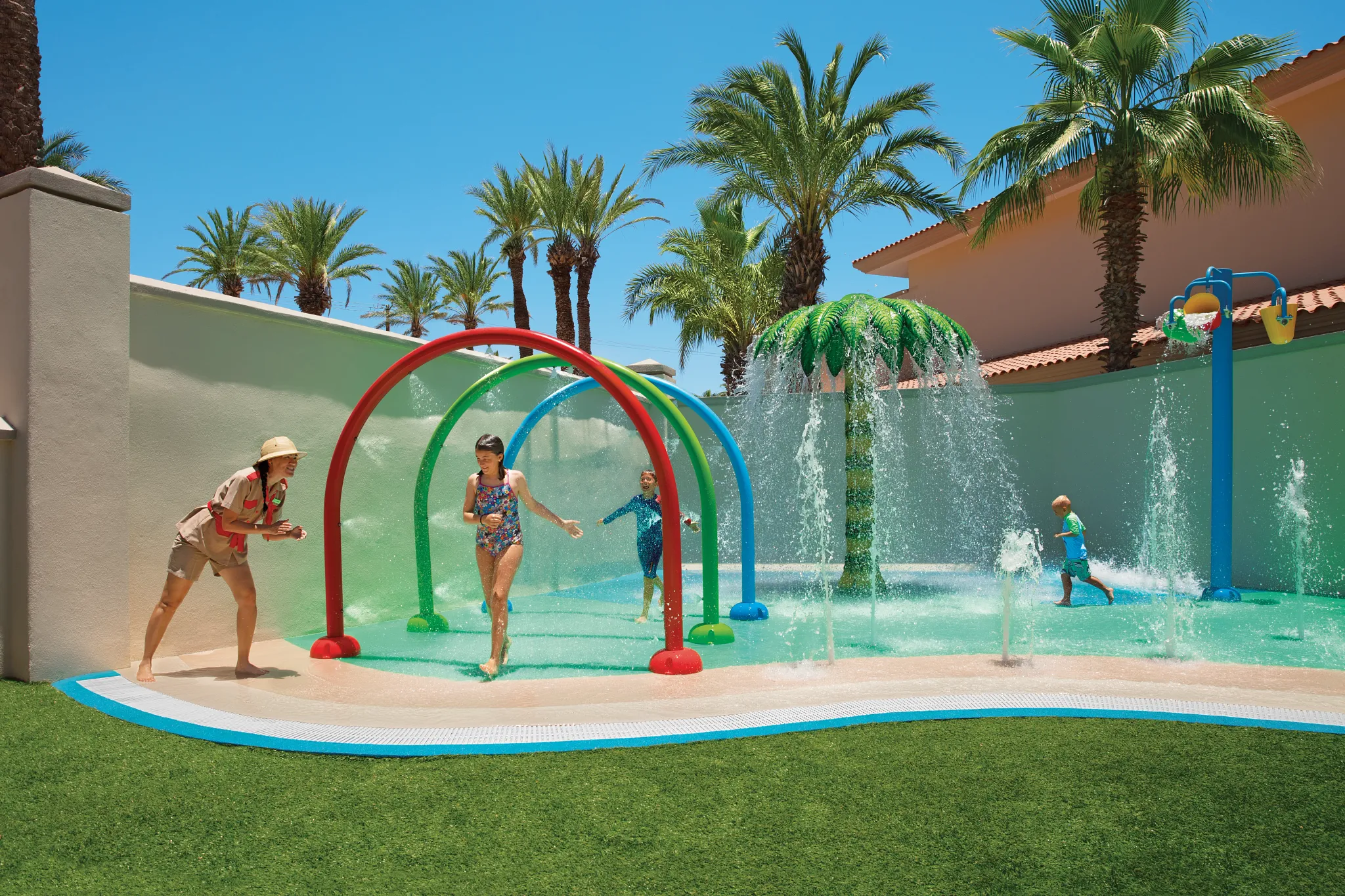 Children playing in a tropical splash zone with water features and palm trees at Dreams Los Cabos Suites Golf Resort & Spa in Los Cabos.