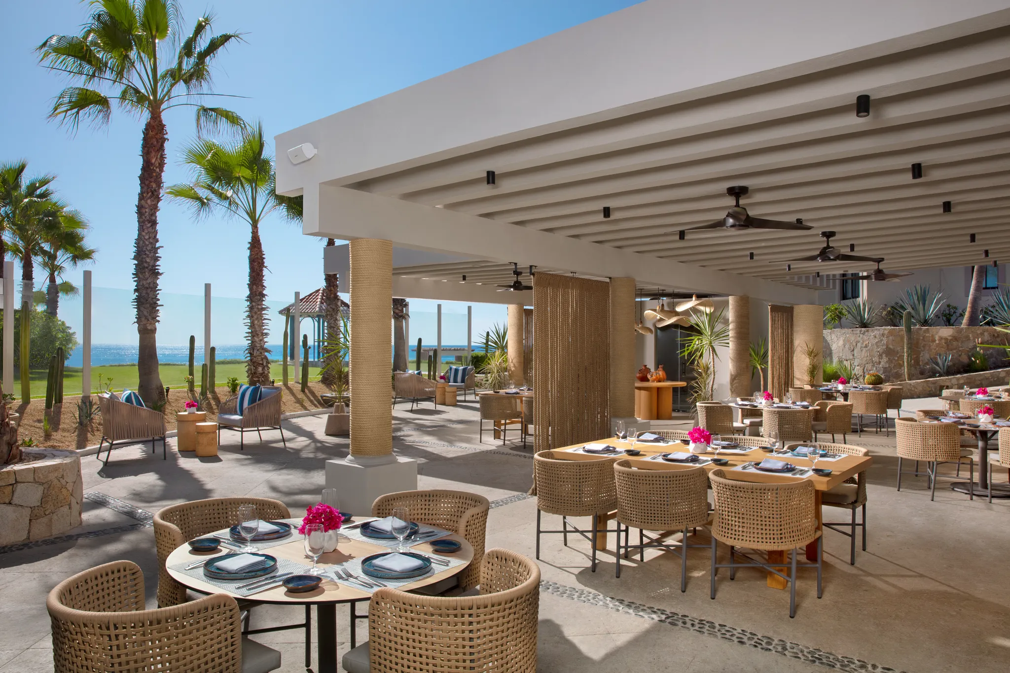 Oceana seafood restaurant at Dreams Los Cabos Suites Golf Resort & Spa featuring open-air oceanfront dining with woven chairs, palm trees, and Sea of Cortez views.