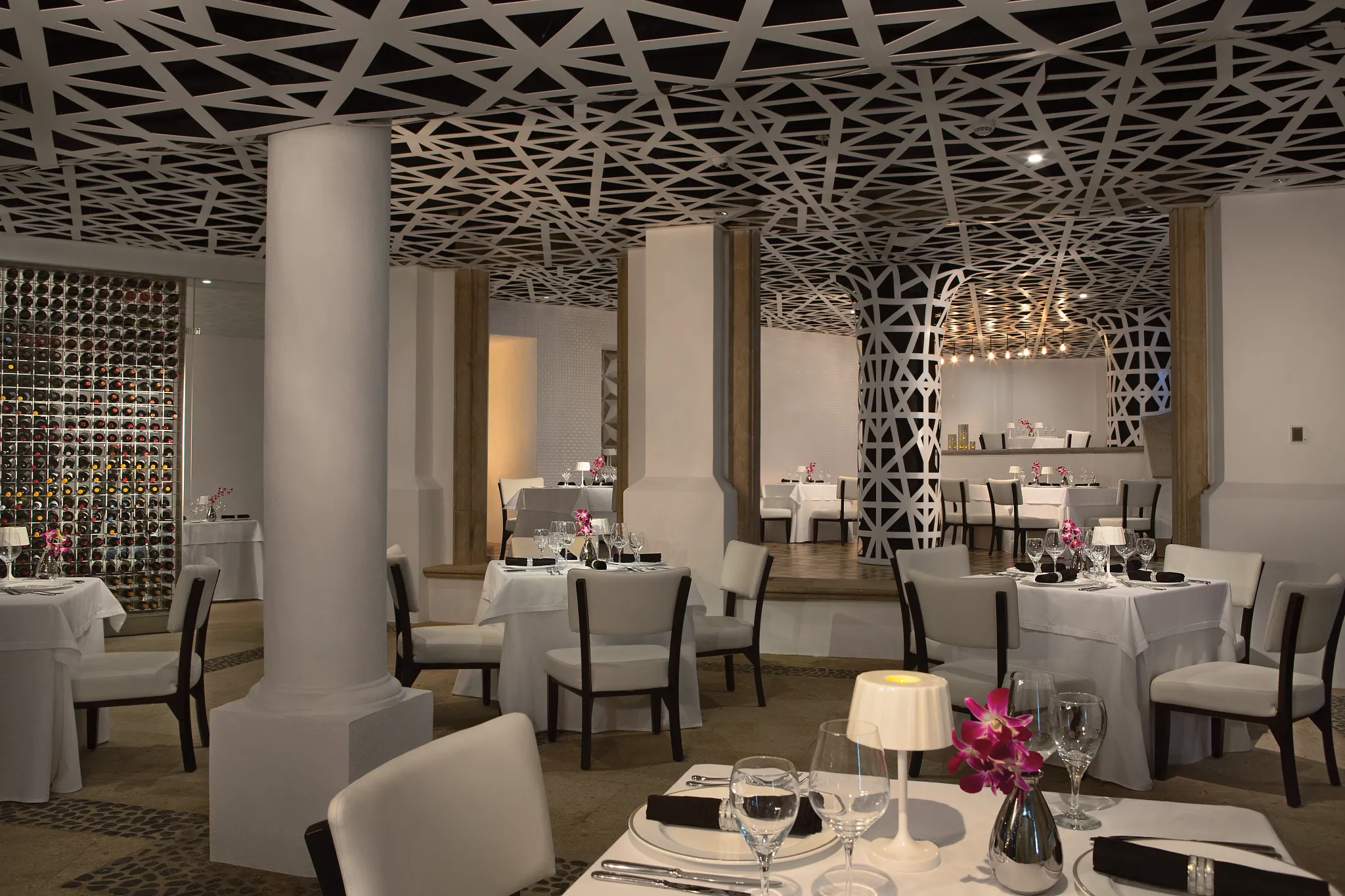 Portofino Mediterranean restaurant at Dreams Los Cabos Suites Golf Resort & Spa featuring elegant white table settings, modern lattice ceiling design, and an extensive wine display.