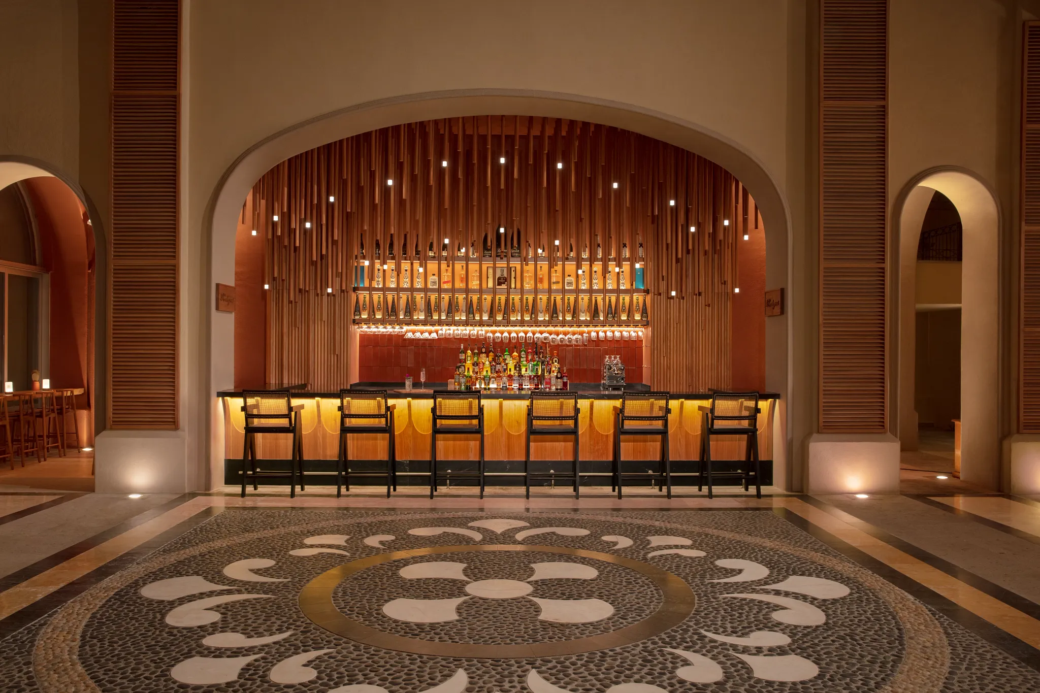 Rendezvous Lobby Bar at Dreams Los Cabos Suites Golf Resort & Spa featuring a stylish arched bar with warm lighting, premium spirits, and elegant seating.