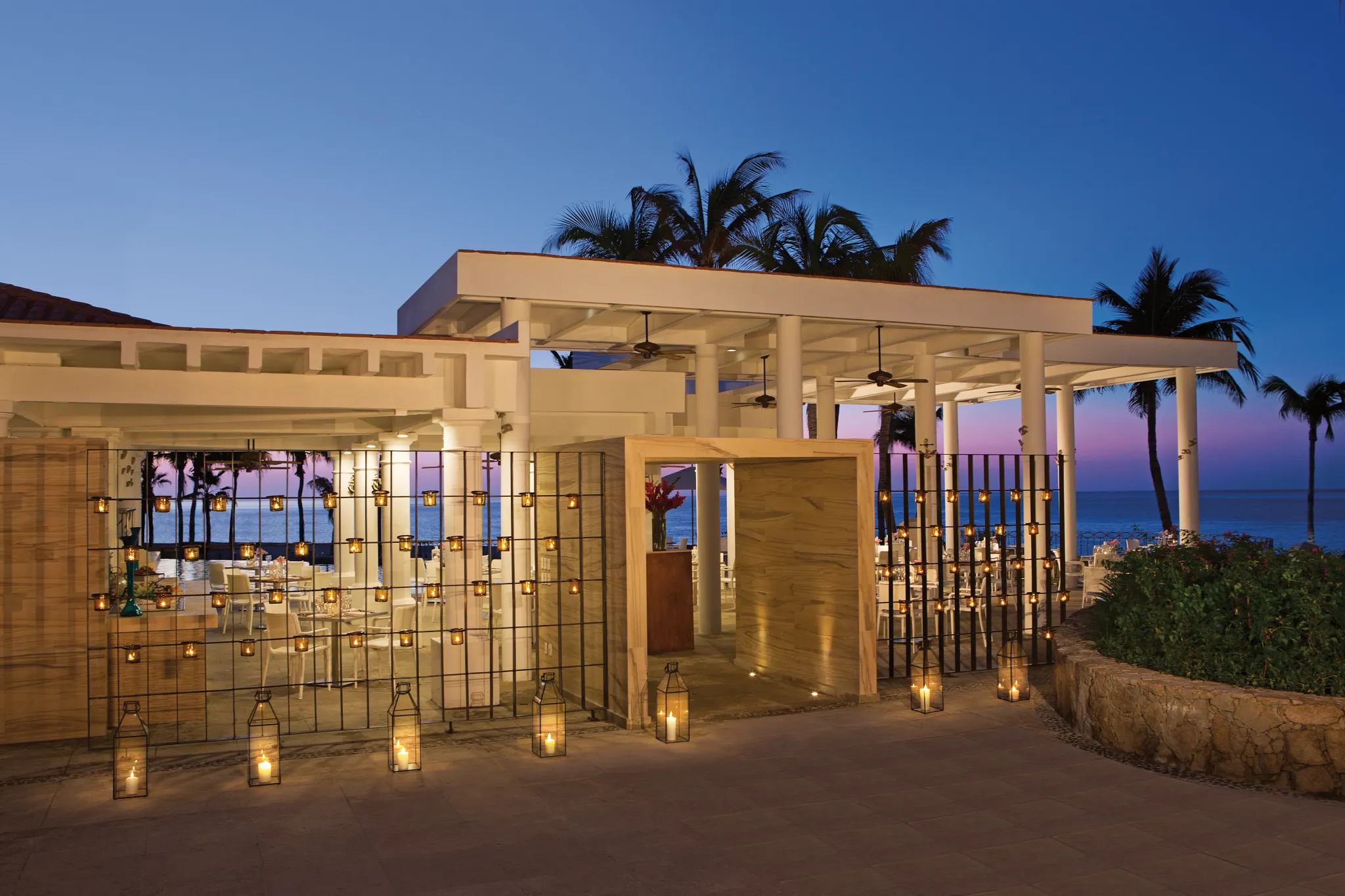 Seaside Grill oceanfront restaurant at Dreams Los Cabos Suites Golf Resort & Spa featuring open-air dining, candlelit ambiance, and views of the Sea of Cortez at sunset.